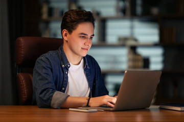 Young guy startuper working at dark office, using laptop