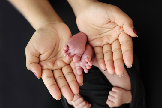 The palms of the parents. A mother hold the feet of a newborn child in a black blanket on a Black background. The feet of a newborn in the hands of parents. Macro Photo of foot, heels and toes
