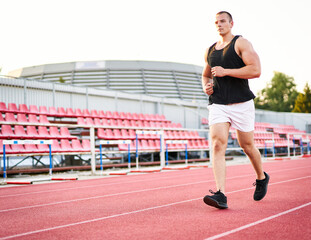 Fototapeta premium Young muscular fit male sprinter running on a red running track - Fitness and wellness concept with a millennial runner - Copyspace on the photo's left side