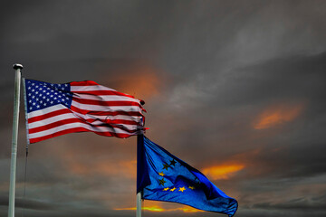 Flag of United states of America higher than flag of Euro union. Dramatic cloudy sunset or sunrise...