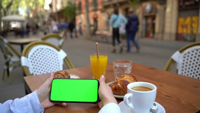 Holding cell phone without touching horizontal  screen. Green monitor chromakey. Woman having breakfast in Barcelona street cafe. Video footage moke up template