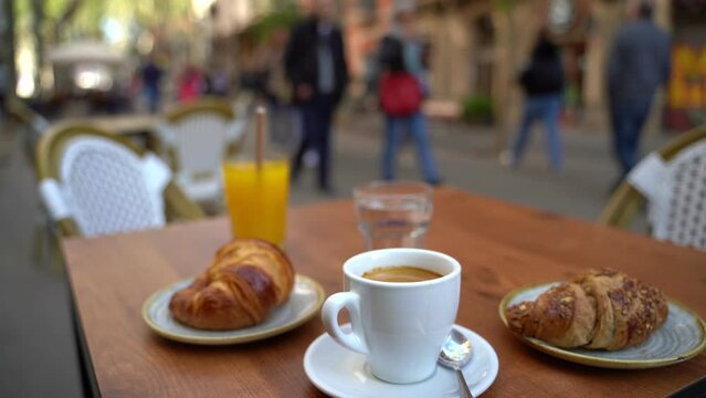 Street outdoor cafe cup of coffee, orange juice, water, croissant. Breakfast out. Passers-by pass by. European street Barcelona video footage
