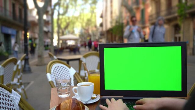 Laptop pc with green chroma key screen working in street cafe. Remote work or online shopping (learning). mock up background. Outside table with croissant, cup of coffee and water. Video footage