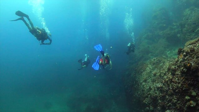 Under water film - Sail Rock island - Thailand - four scuba divers along side coral reef - camera following from behind