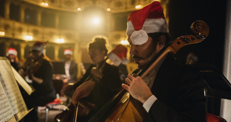 Cinematic Shot of Symphony Orchestra Musicians Wearing Santa Hats and Performing on the Stage of a Classic Theatre During a Classical Music Concert. Focused Performers Playing Different Instruments © Kitreel