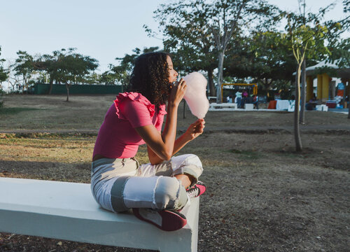 Beautiful afro girl having fun in the park and eating cotton candy. Happy black woman smiling in the park, Lifestyle. Concept of people and happiness.