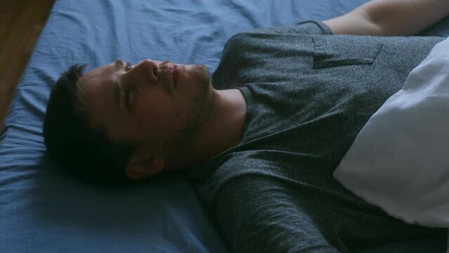 Depression man. On the bed covered with bed linen lies a disappointment male, he looks indifferently at one point.