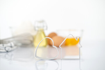 Dessert ingredients and utensils on white reflect table background . Front view. Copy space. egg, flour, milk, oil, Whisk, cookies cutter.