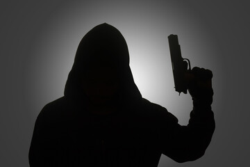 Mysterious man wearing black hoodie holding a pistol, shooting with a gun. Silhouette and dark...