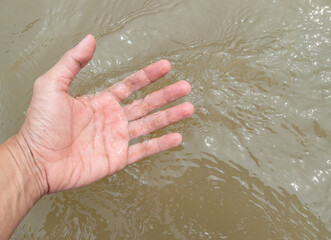 Fototapeta premium The hand of a young man is touching the flowing water.