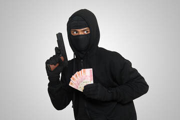 Portrait of mysterious man wearing black hoodie and mask doing shooting with gun while holding one...