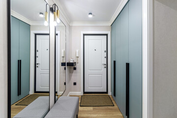 White entrance door in a modern renovated hallway with large mirrors and wardrobe