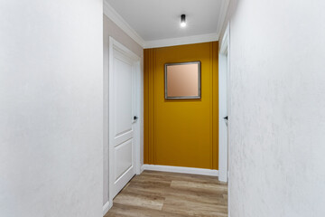 White door to the room at the end of a long corridor with a yellow wall and a painting