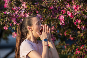 Girl sneezing in front of blooming tree in spring