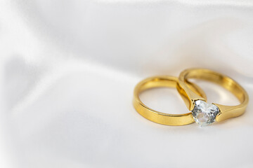 Festive wedding background with two gold rings with diamond on white satin material. Copy space.