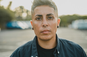 Portrait of Hispanic female with round black ear studs and in casual clothes looking at camera while standing on blurred city street during daytime