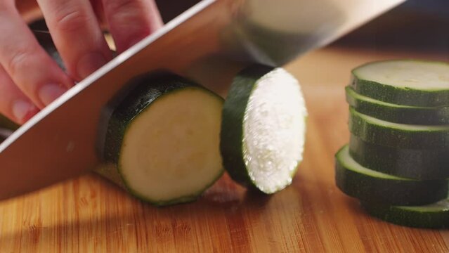 Chef cutting fresh zucchini on wooden board, close up macro of squash courgette.