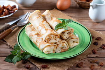 Rolled pancakes with cottage cheese and raisins on rustic wooden table