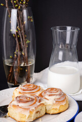 cinnamon rolls on white plate with blue rim decorated with rosemary and jug of milk
