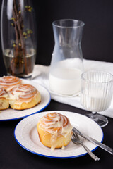 cinnamon rolls on white plate with blue rim decorated with rosemary and jug of milk
