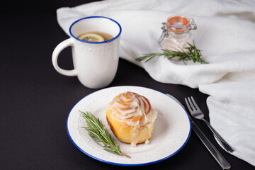 homemade cinnamon rolls on white ceramic plates decorated with rosemary and a cup of tea