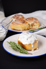 cinnamon rolls on white plate with blue rim decorated with rosemary and jug of milk