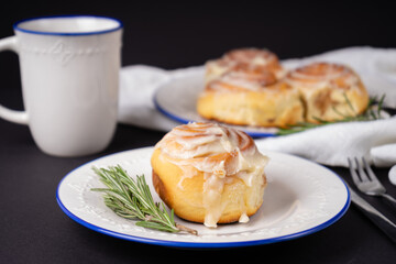 homemade cinnamon rolls on white ceramic plates decorated with rosemary and a cup of tea