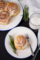 cinnamon rolls on white plate with blue rim decorated with rosemary and glass of milk