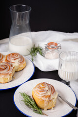 cinnamon rolls on white plate with blue rim decorated with rosemary and jug of milk