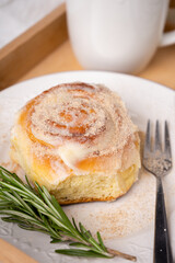 closeup of a cinnamon roll on a white plate with rosemary and spices