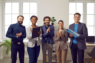 Diverse business team standing in the office, smiling and clapping hands. Group of happy, positive...