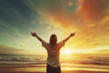 A happy woman greeting the sun with raised arms at the beach