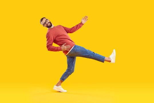 Cheerful, funny and humorous young man takes big wide step on orange background. Handsome stylish man in casual sweatshirt, jeans and sneakers is taking step while looking at camera. Full length.