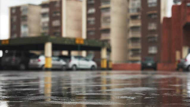 Close-up of rain drops on the pavement of multi-level parking lots. Copy space blurred background with residential buildings and parked cars. Cloudy weather in the city