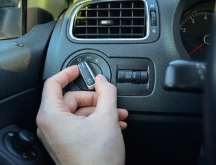 The driver's hand turning the toggle switch on the low beam on the dashboard of the car © Rinat Akhtiamov
