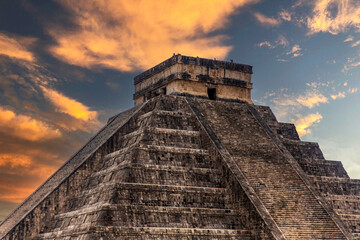 The pyramid of Chichen Itza in honor of the God Kukulkan under a beautiful tropical orange sunset,...