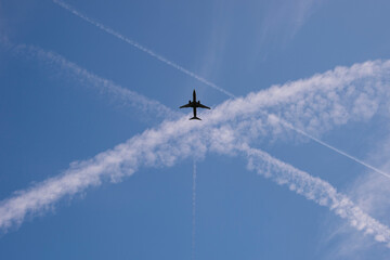 Airplane in a blue sky with crossing vapour trails