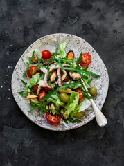 Salad with arugula, cherry tomatoes and seafood on a dark background, top view