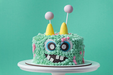 Monster theme cake on the turquoise background. Funny birthday cake with turquoise fluffy cream...