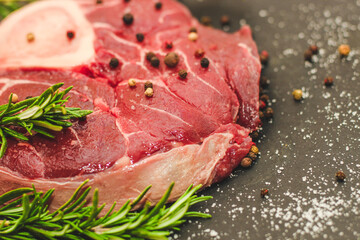 Fresh piece of meat large beef steak on the bone ossobuco with a sprig of rosemary on a black background.