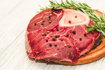 Fresh piece of meat large beef steak on the bone ossobuco with pepper, rosemary on the board.