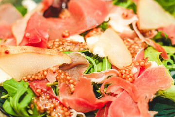 Salad with herbs, arugula, prosciutto, cheese, green olives and nuts.