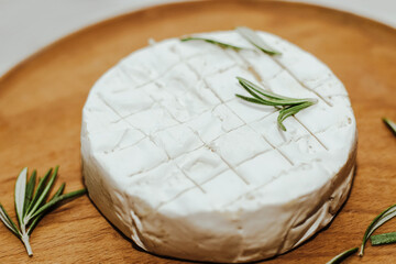 Round cheese in camembert mold with a sprig of rosemary on the table.