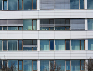 Fragment of a modern glass office building. Background with windows with blinds. City office building with blue sky in background.