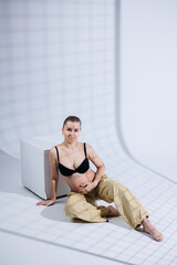 Young happy pregnant woman in bra and pants on white background. Happy pregnancy. Stylish pregnant woman poses in the studio