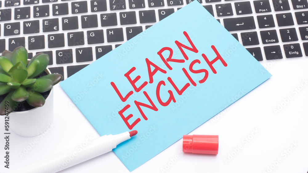 Aufkleber text learn english is written in red marker on a blue card. in the frame is a laptop keyboard and a 