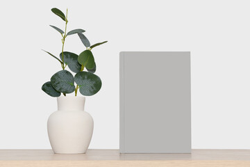 Mockup of a gray book and a gray vase with green eucalyptus branches.