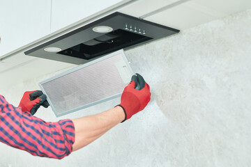 Mans hands removing a filter from cooker hood for cleaning or service. Replacing filter in kitchen...