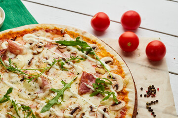 Freshly baked pizza with ham, rukkola and mushrooms served on wooden background with tomatoes, sauces and herbs. Food delivery concept. Restaurant menu