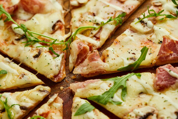 Sliced Freshly baked pizza with ham, rukkola and mushrooms served on wooden background with tomatoes, sauces and herbs. Food delivery concept. Restaurant menu